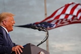 Trump opens his mouth to speak at a podium and an America flag billows behind him, looking like it's coming out of his mouth