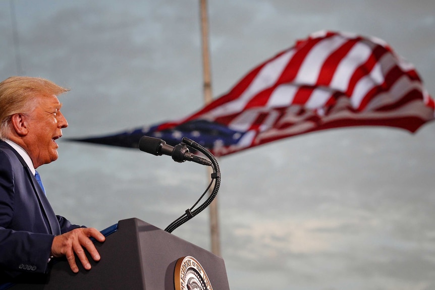 Trump opens his mouth to speak at a podium and an America flag billows behind him, looking like it's coming out of his mouth