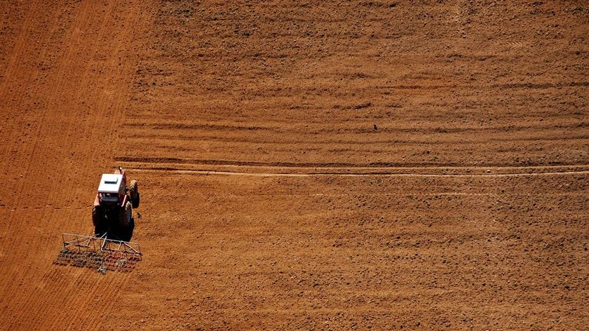 A tractor pulling a plough in the middle of a barren field.