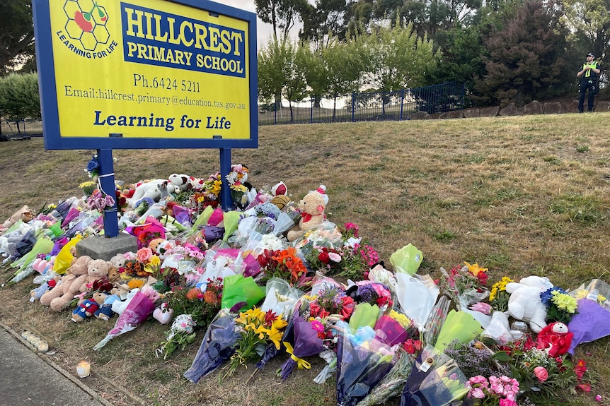 Flowers and soft toys lie at the base of the primary school sign