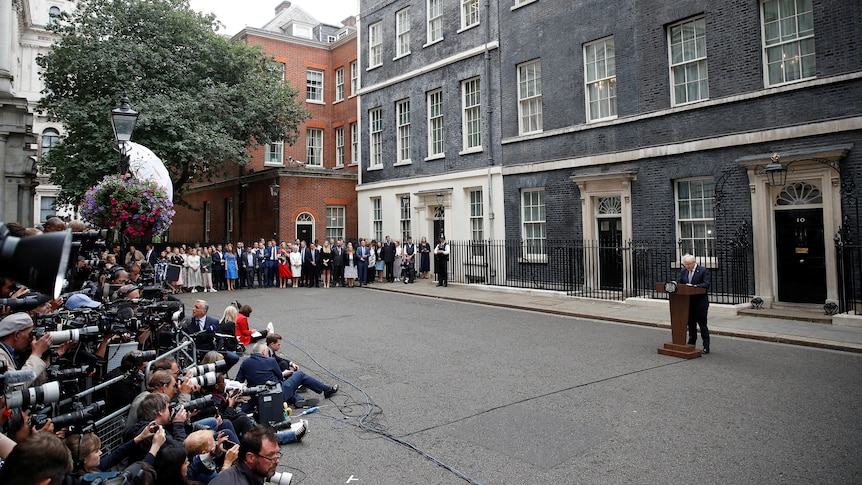 Media and Downing Street staff listen as Boris Johnson speaks at a lectern.