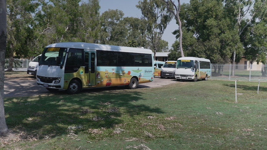 5 small school buses parked near grass and a fence