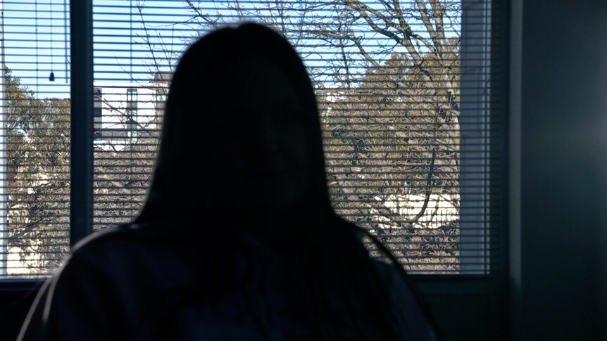 An unidentifiable woman looks out a window, seen from behind.