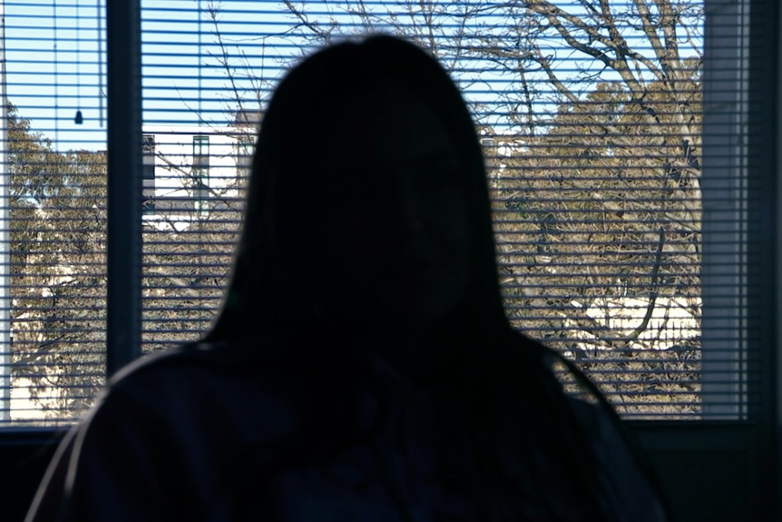 An unidentifiable woman looks out a window, seen from behind.