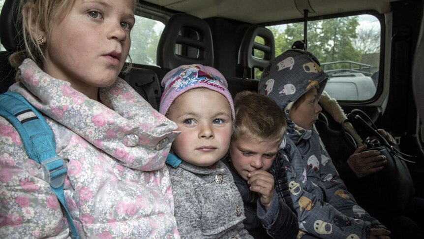 four children sit of the back of a car awaiting evacuation