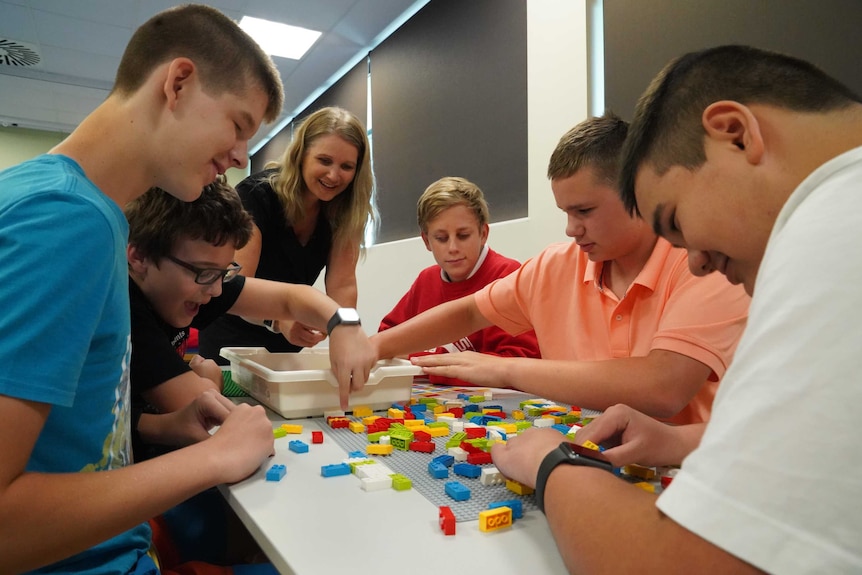 A group of five students and Melissa sit around a table and work with the braille bricks.