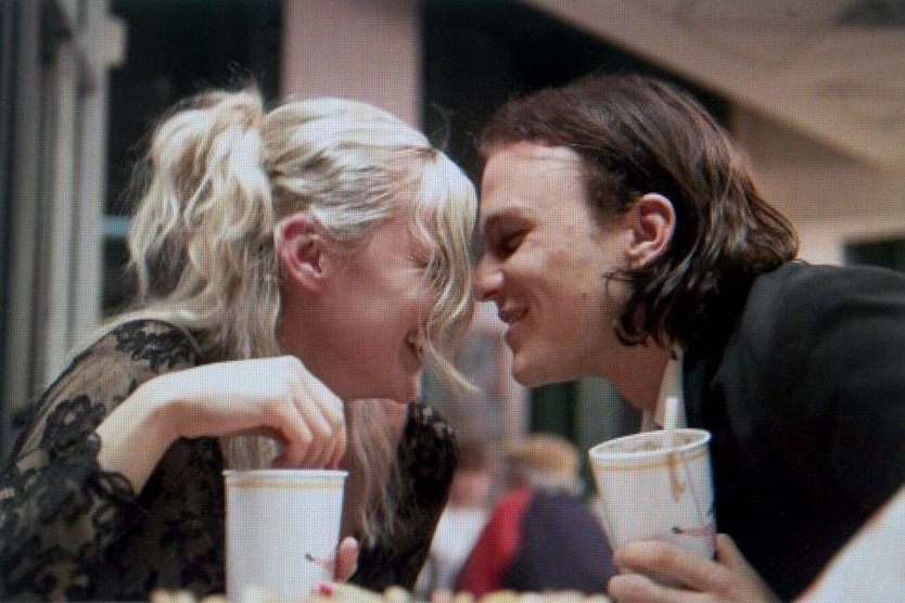 A movie still of a couple sitting across from each other at table, about to lock lips