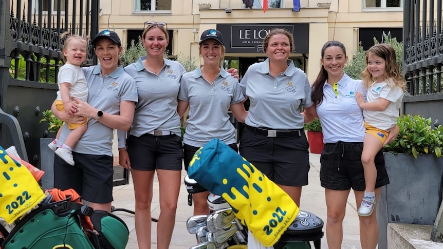 Five women stand in front of a motel in France and pose for a photograph with their children and golf bags.