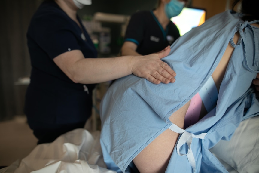 A close-up of a midwife placing her hand on Taryn's back, as she kneels in labour.