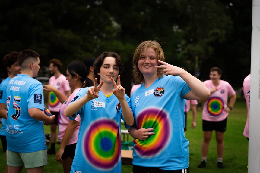 Two young people wearing blue shirts with rainbow circles hold up their hands to make peace signs.