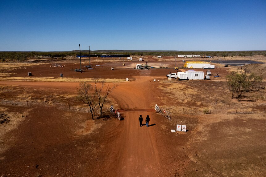 An aerial view of two men walking down a red dirt track towards a fracking exploration site.