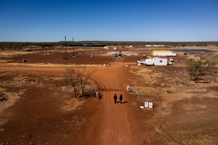 An aerial view of two men walking down a red dirt track towards a fracking exploration site.