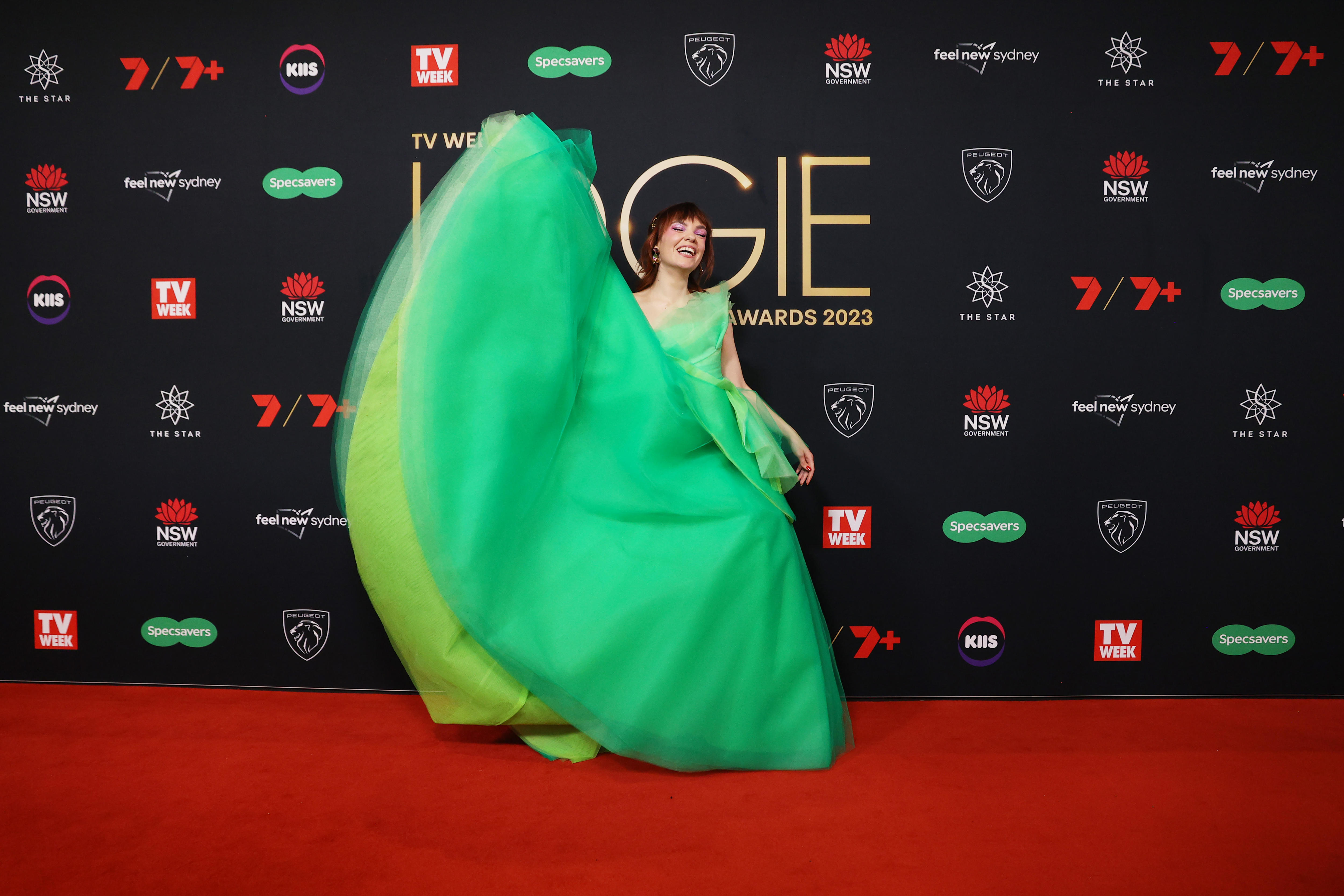 La actriz con un vestido verde que fluye, levanta la parte inferior sobre su cabeza mientras sonríe