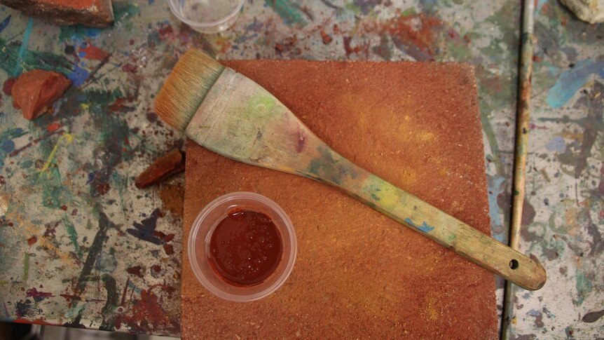 A brush and a pot of ochre on top of a brick at the Wujal Wujal arts centre, viewed from above