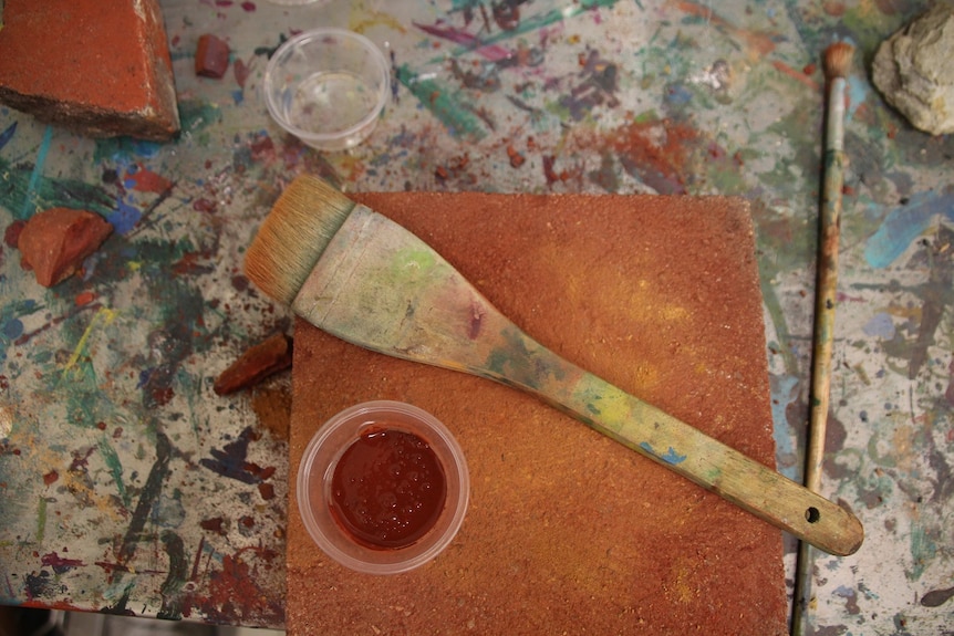 A brush and a pot of ochre on top of a brick at the Wujal Wujal arts centre, viewed from above