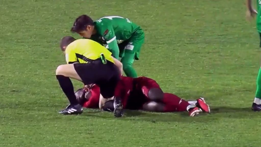 A soccer referee and player assist an injured player.