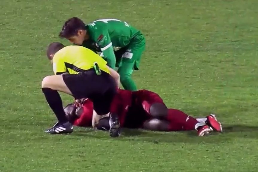 A soccer referee and player assist an injured player.
