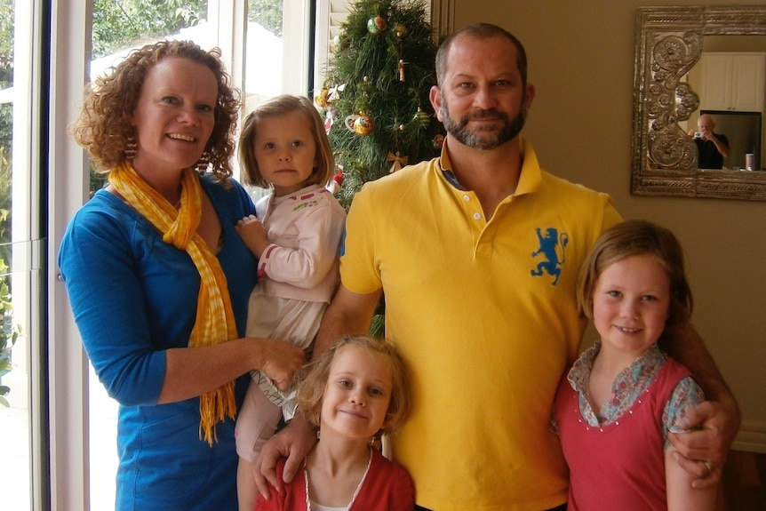 A family of five pose for a photo in front of a Christmas tree.