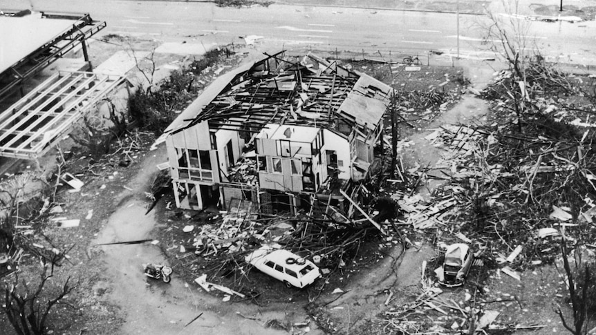 View from above of a house whose roof has been torn off and walls smashed, and surrounded by rubble.