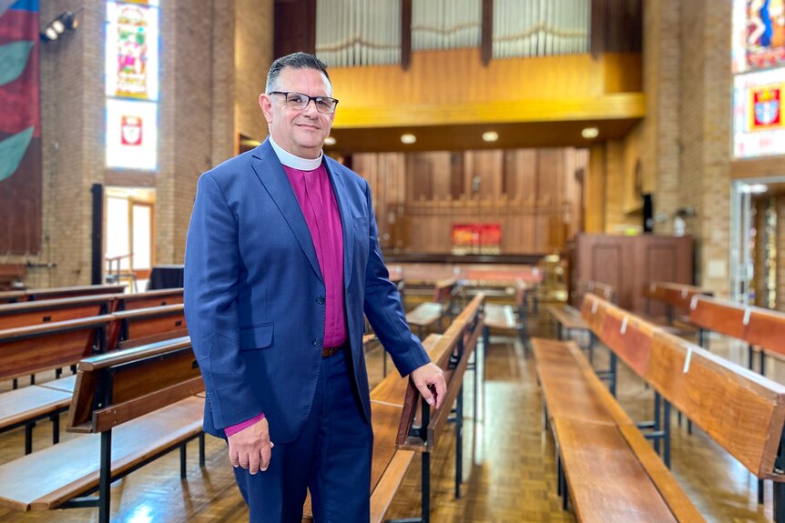 an Anglican bishop stands near a pew in a church