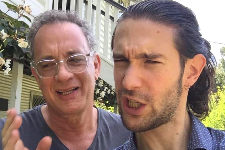 Actor Tom Hanks with another man outside a wooden cabin