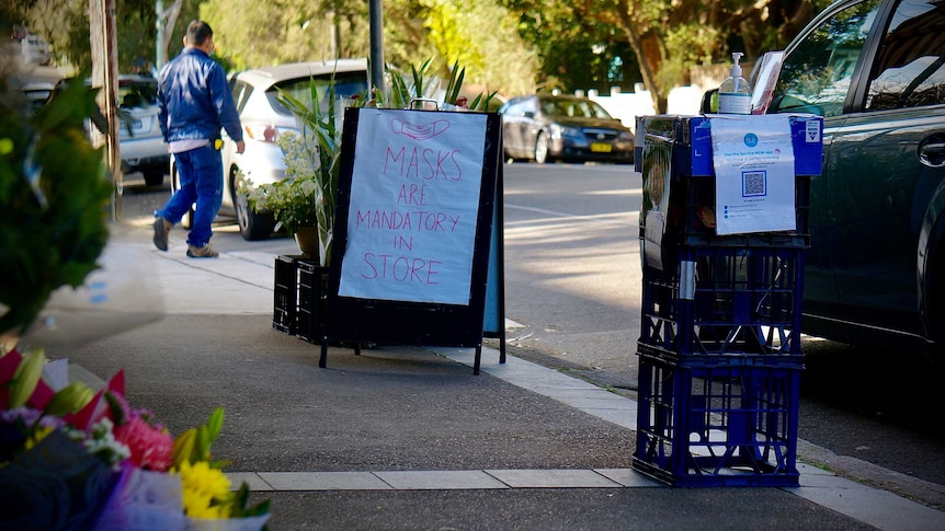 A sign about mandatory masks and a QR check-in and sanitising station outside a Sydney supermarket.