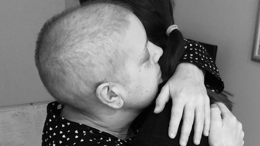 A black and white image of a woman with shaved head hugging her daughter.