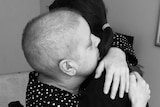 A black and white image of a woman with shaved head hugging her daughter.