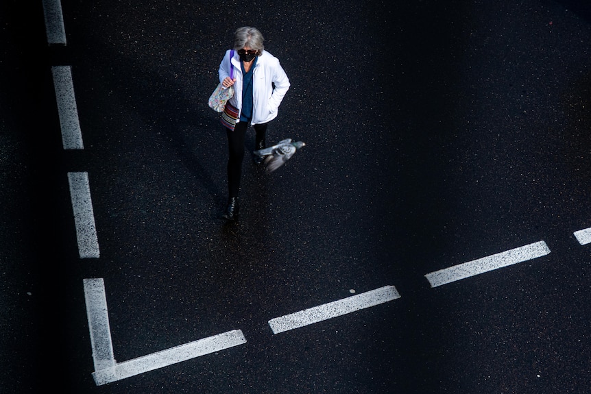 An aerial view of a person wearing a face mask crossing a road with white markings on it