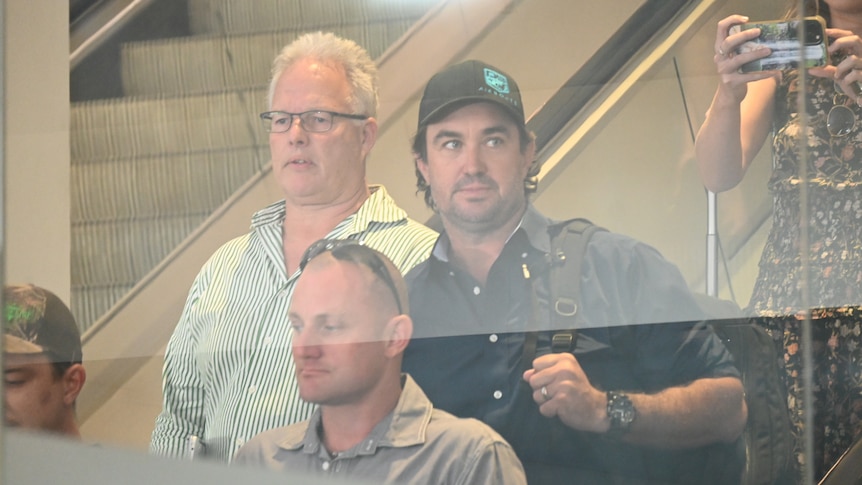 Celebrity crocodile wrangler Matt Wright descending an escalator at Darwin Airport, surrounded by an entourage.