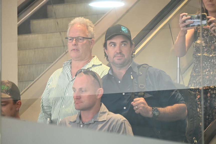 Celebrity crocodile wrangler Matt Wright descending an escalator at Darwin Airport, surrounded by an entourage.