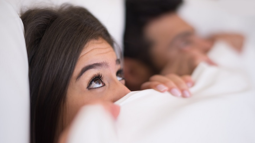 Young women lies in bed looking anxious.