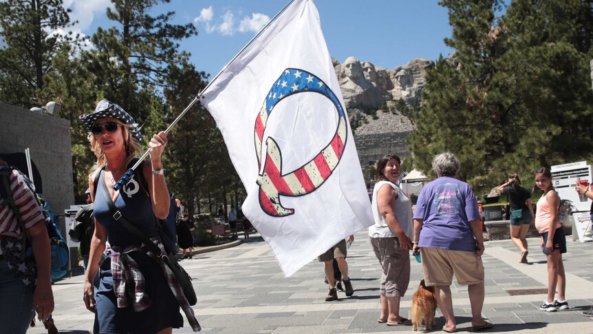 A woman in a cowboy hat carries a white flag with a "Q" on it.