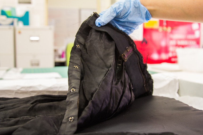 Black gown held by curators hands in gloves.