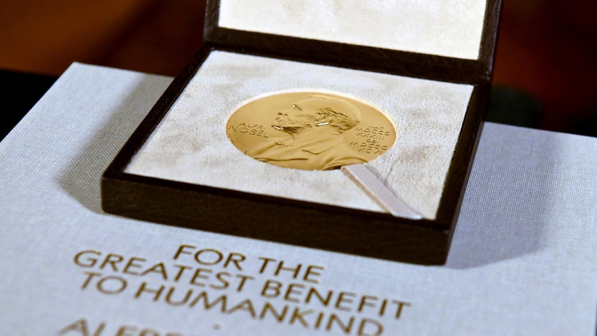 A close-up photo shows a golden medal in a case on top of a sheet of paper.