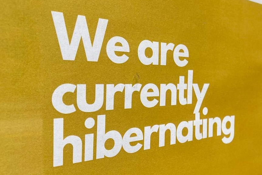 A yellow sign posted outside a business says "we are currently hibernating".