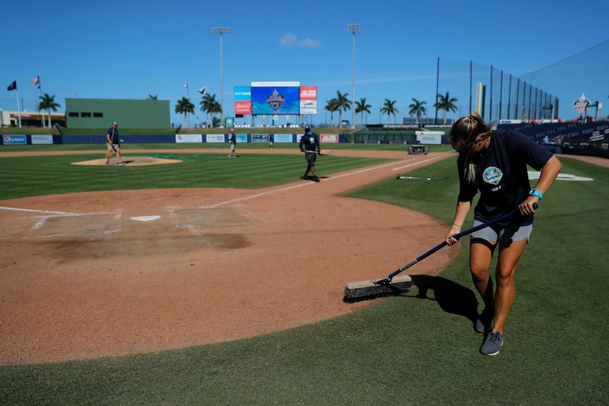 A worker runs a broom over the dirt at home plate after a baseball game.