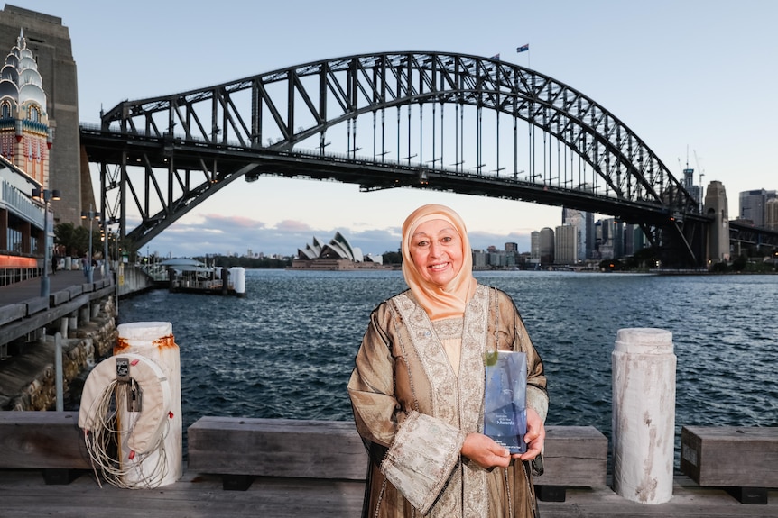 Woman holding trophy before the Sydney Harbour Bridge and the Sydney Opera House
