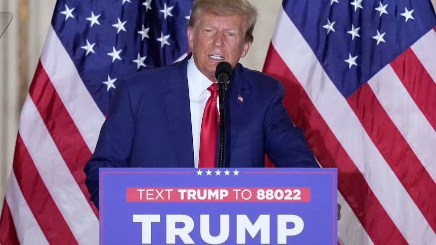 Donald Trump dressed in a suit stands behind a podium as he speaks at Mar-a-Lago