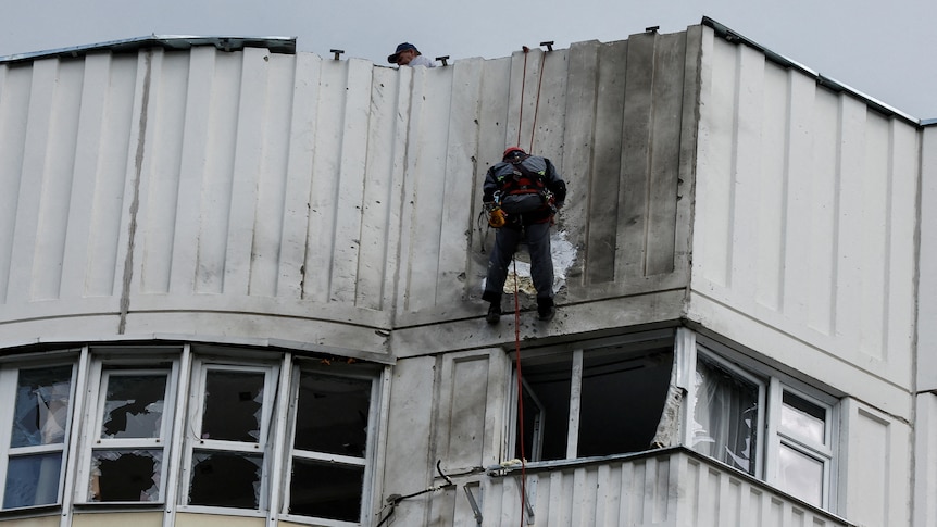 A worker abseils against a building to inspect drone damage. 