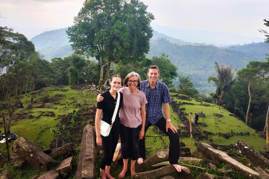 A group of a white man and two white women pose in front of a forest.