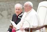 Pope Francis speaks into a microphone while reading from a sheet of paper