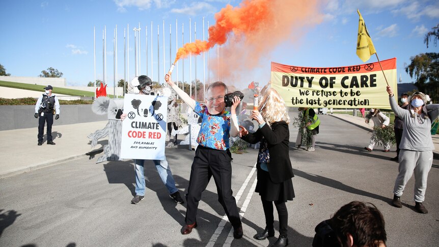 A man in a Scott Morrison mask waves a smoking flare outside Parliament House, as others hold signs and flags.