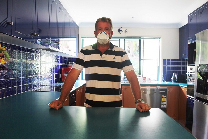 A man wearing a face mask stands in his kitchen