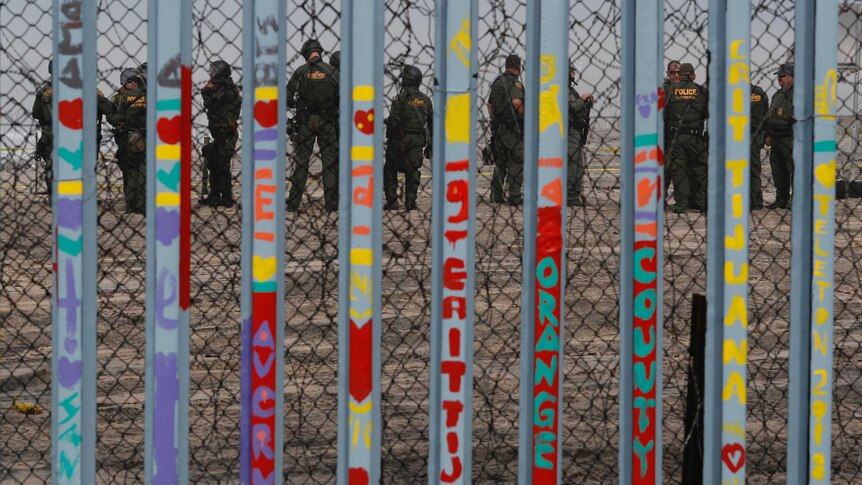 U.S. Border Patrol agents stand guard on the other side of the border as seen through graffitied barred fence