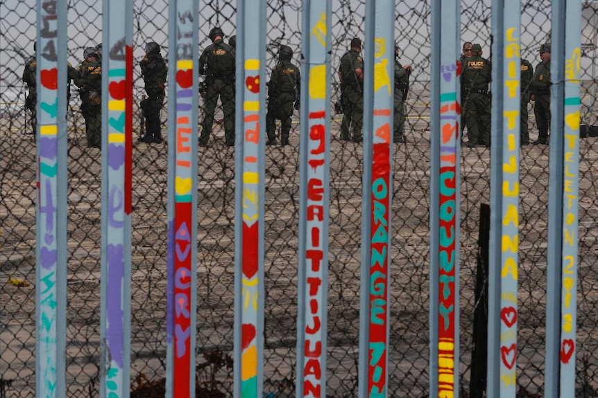 U.S. Border Patrol agents stand guard on the other side of the border as seen through graffitied barred fence