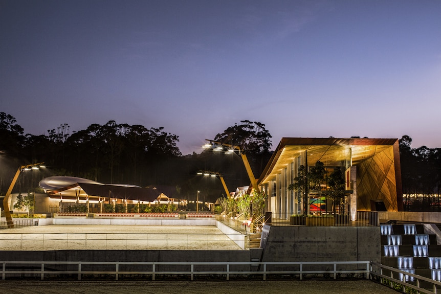 Outdoor equestrian centre with large floodlights and a pavilion to the left.