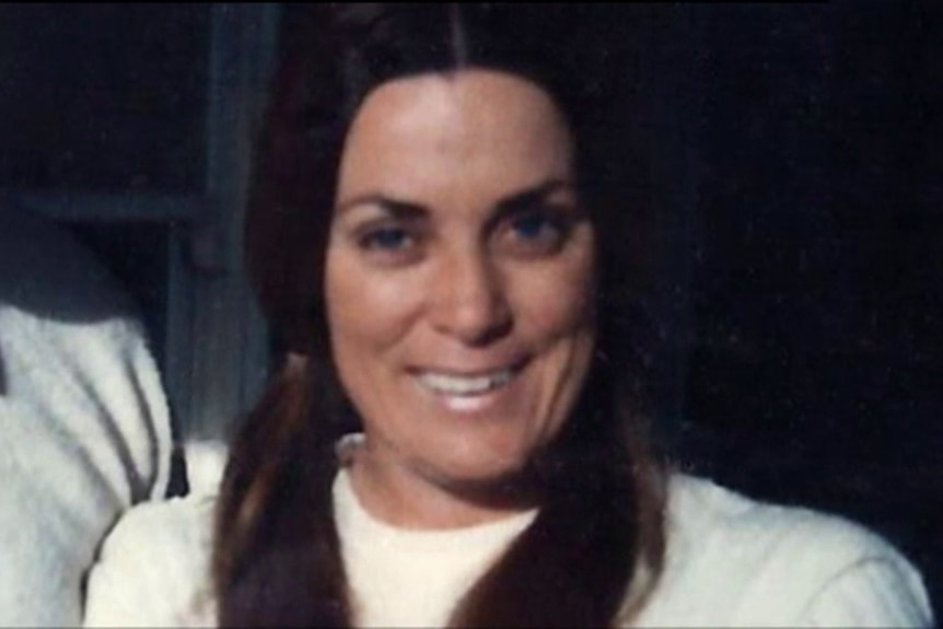 A woman with brown ponytails and blue eyes wearing a white shirt and smiling at the camera.