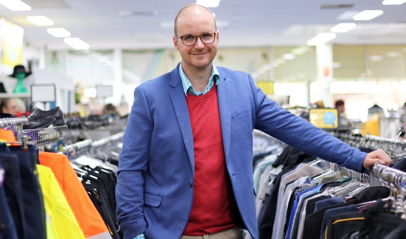 A man in a blue jacket stands between two clothes racks