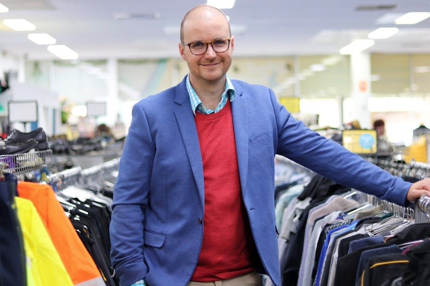 A man in a blue jacket stands between two clothes racks